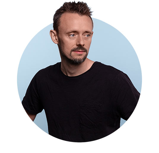 Portrait des Mitarbeiters Nils vor hellblauem Hintergrund